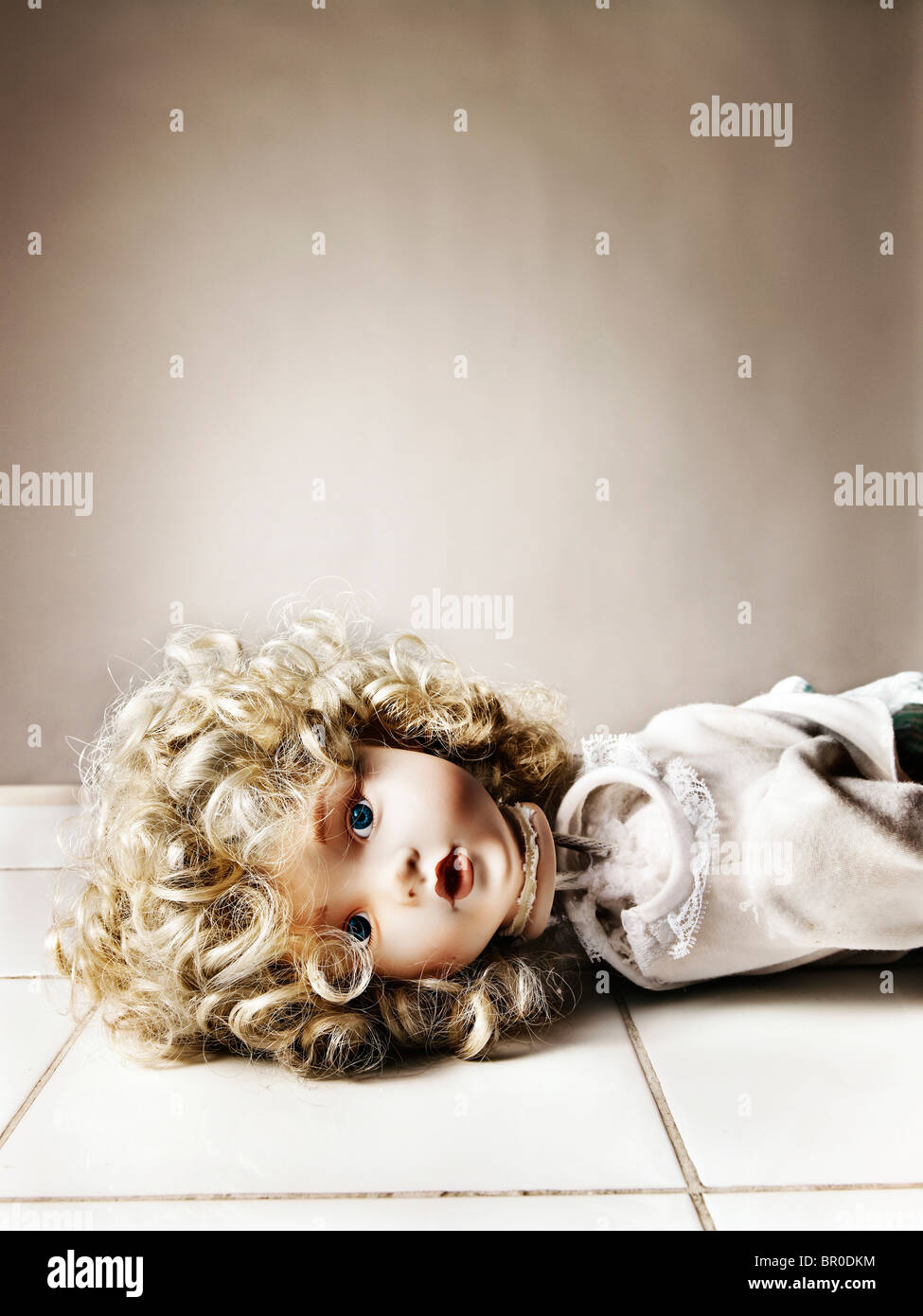 Bambola porcellana con un collo spezzato giacente su un pavimento piastrellato di bianco Foto Stock