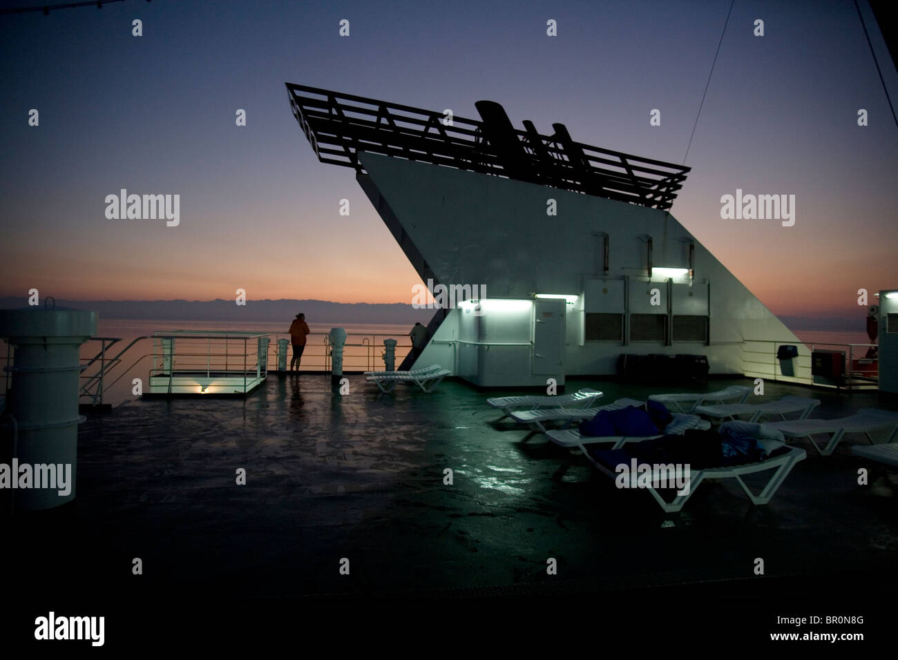 Sul ponte di una trans-Adriatic car ferry crossing un viaggiatori avventurosi orologi il tramonto sul mare calmo. Foto Stock