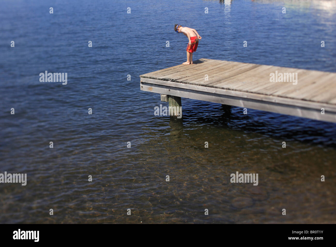 Un giovane ragazzo si erge sulla estremità di un dock guardando oltre il bordo sul lago Payette, McCall, Idaho. Foto Stock