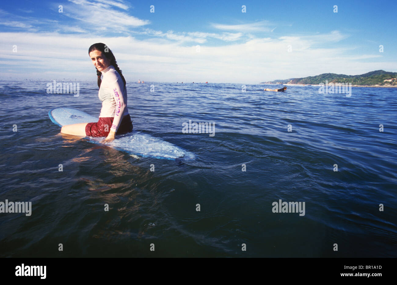 Una giovane donna seduta su una tavola da surf si è rivolta a guardare la fotocamera, Michoacan, Messico. Foto Stock