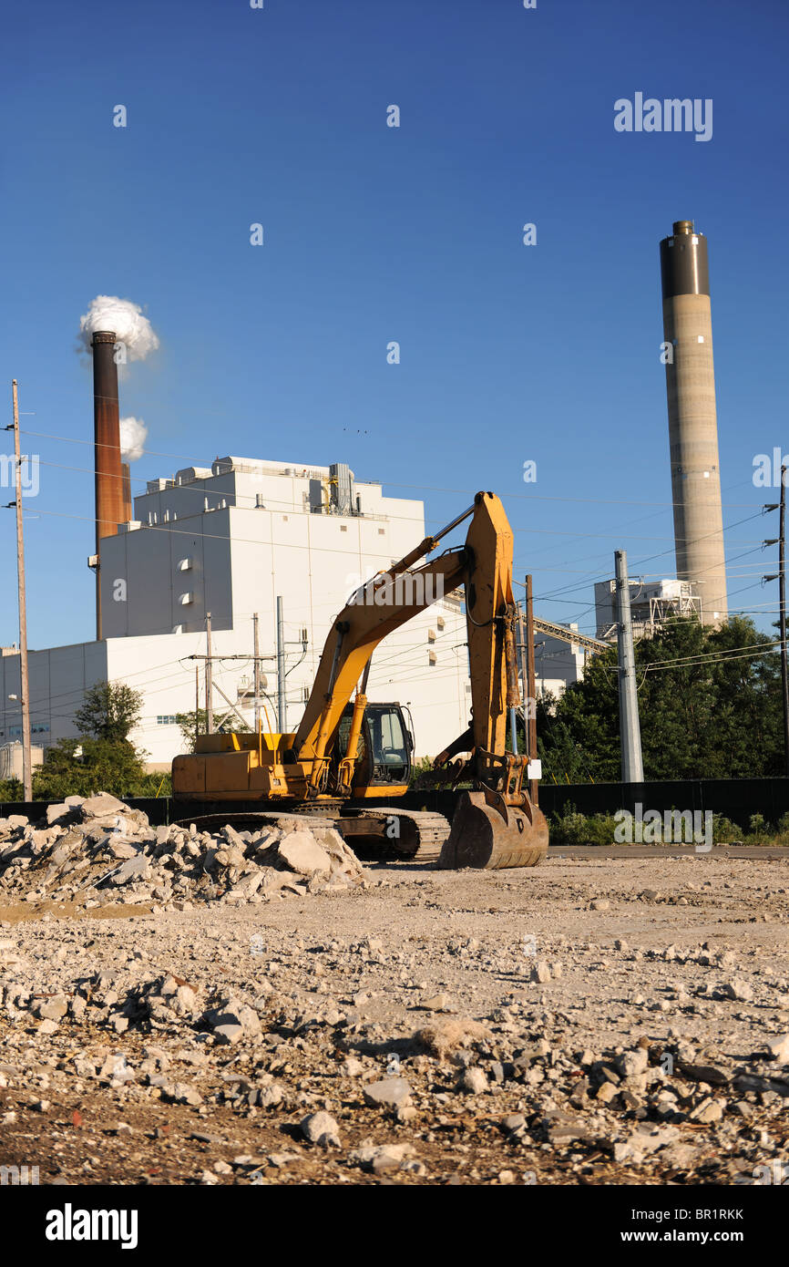 Sito industriale con un bulldozer in primo piano e fabbrica con fumaioli in background Foto Stock