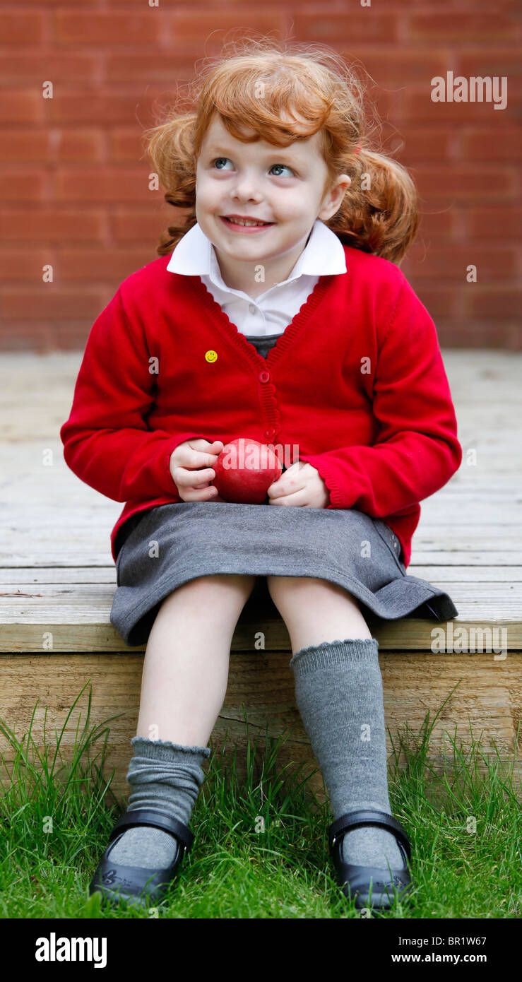 Bambina di 4 anni, indossando la sua uniforme scolastica in un giardino. Foto Stock