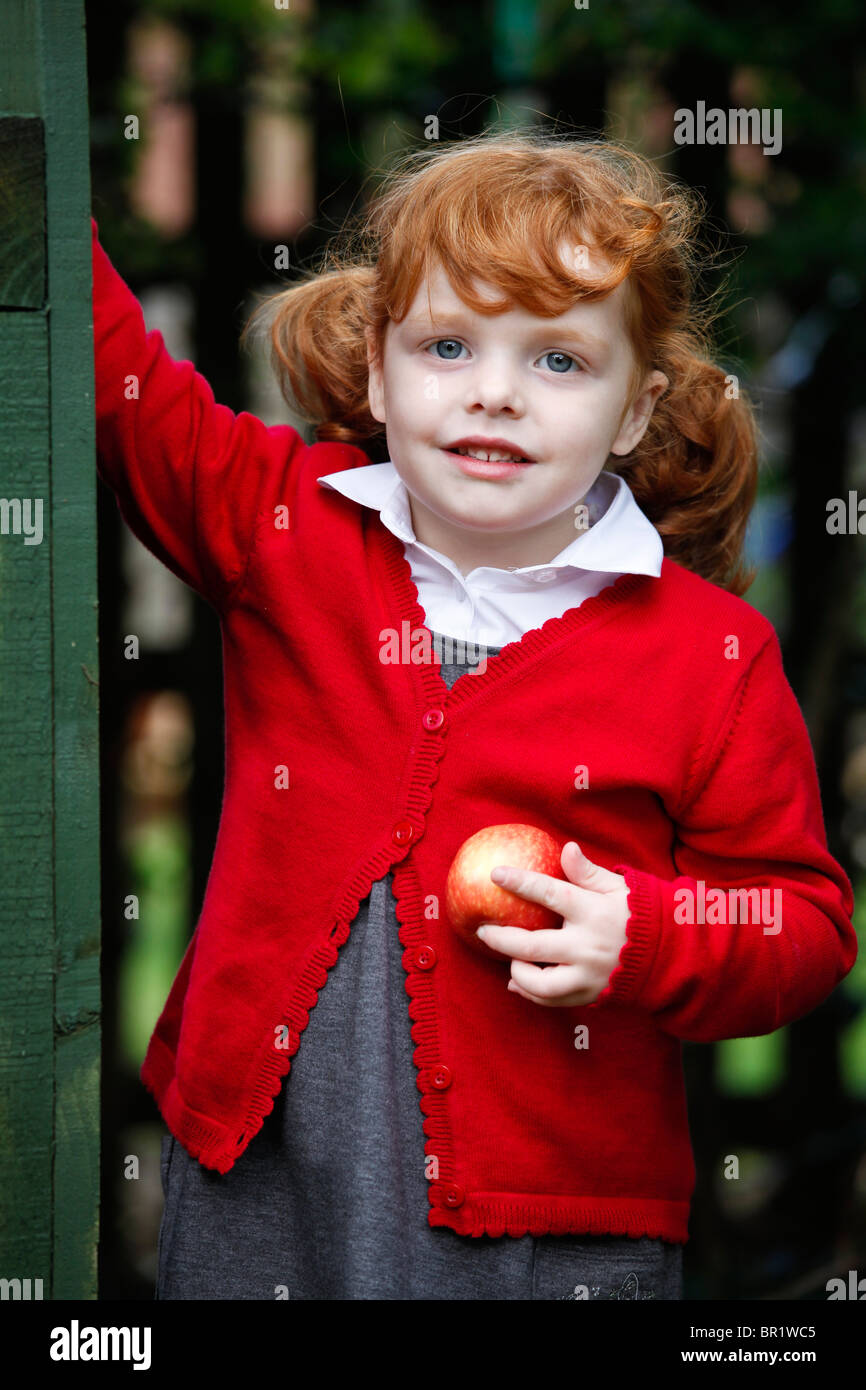 Bambina di 4 anni, indossando la sua uniforme scolastica in un giardino. Foto Stock