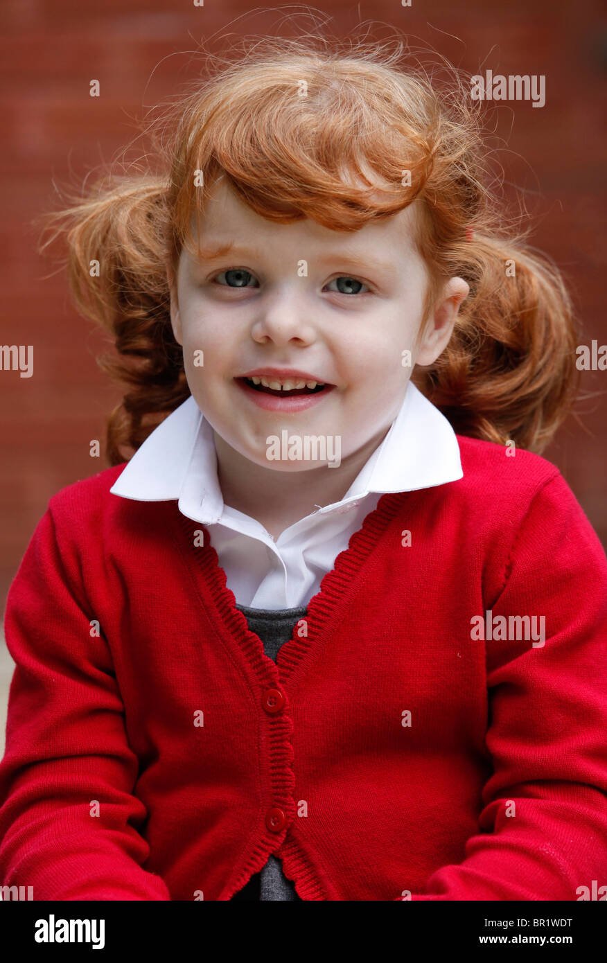 Bambina di 4 anni, indossando la sua uniforme scolastica in un giardino. Foto Stock