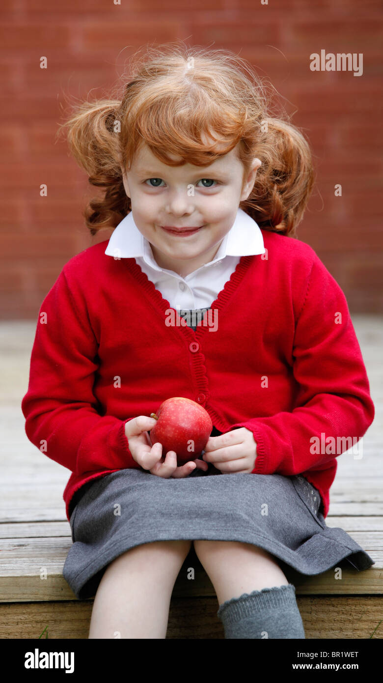 Bambina di 4 anni, indossando la sua uniforme scolastica in un giardino. Foto Stock