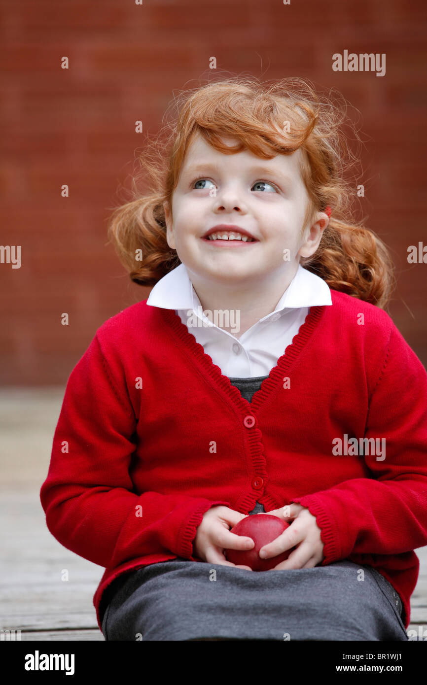 Bambina di 4 anni, indossando la sua uniforme scolastica in un giardino. Foto Stock