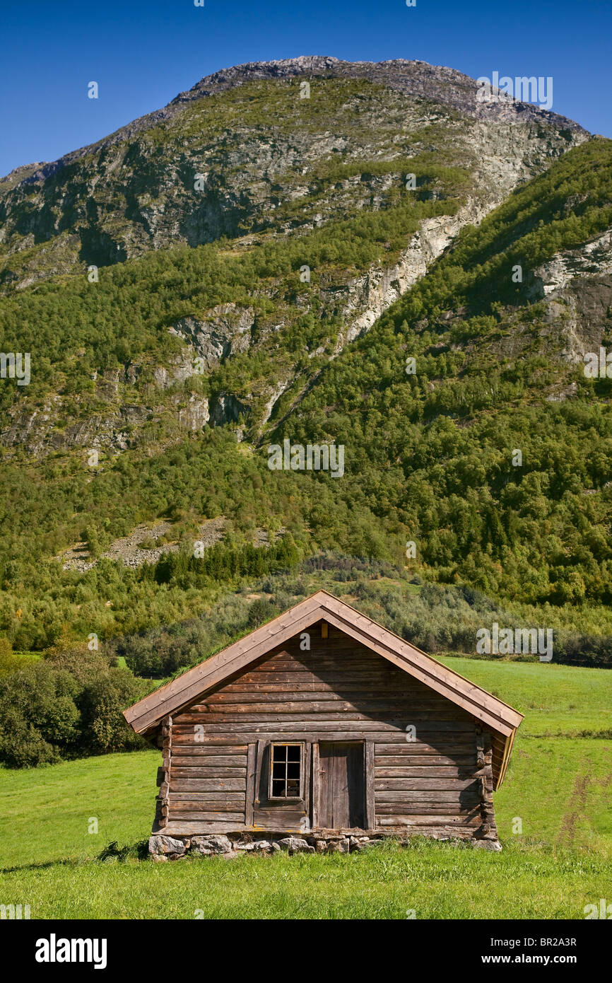 Alpine imbarcati in legno capanna, maggese prato con cascata di collina in background, Olden, Norvegia. Sole brillante Foto Stock
