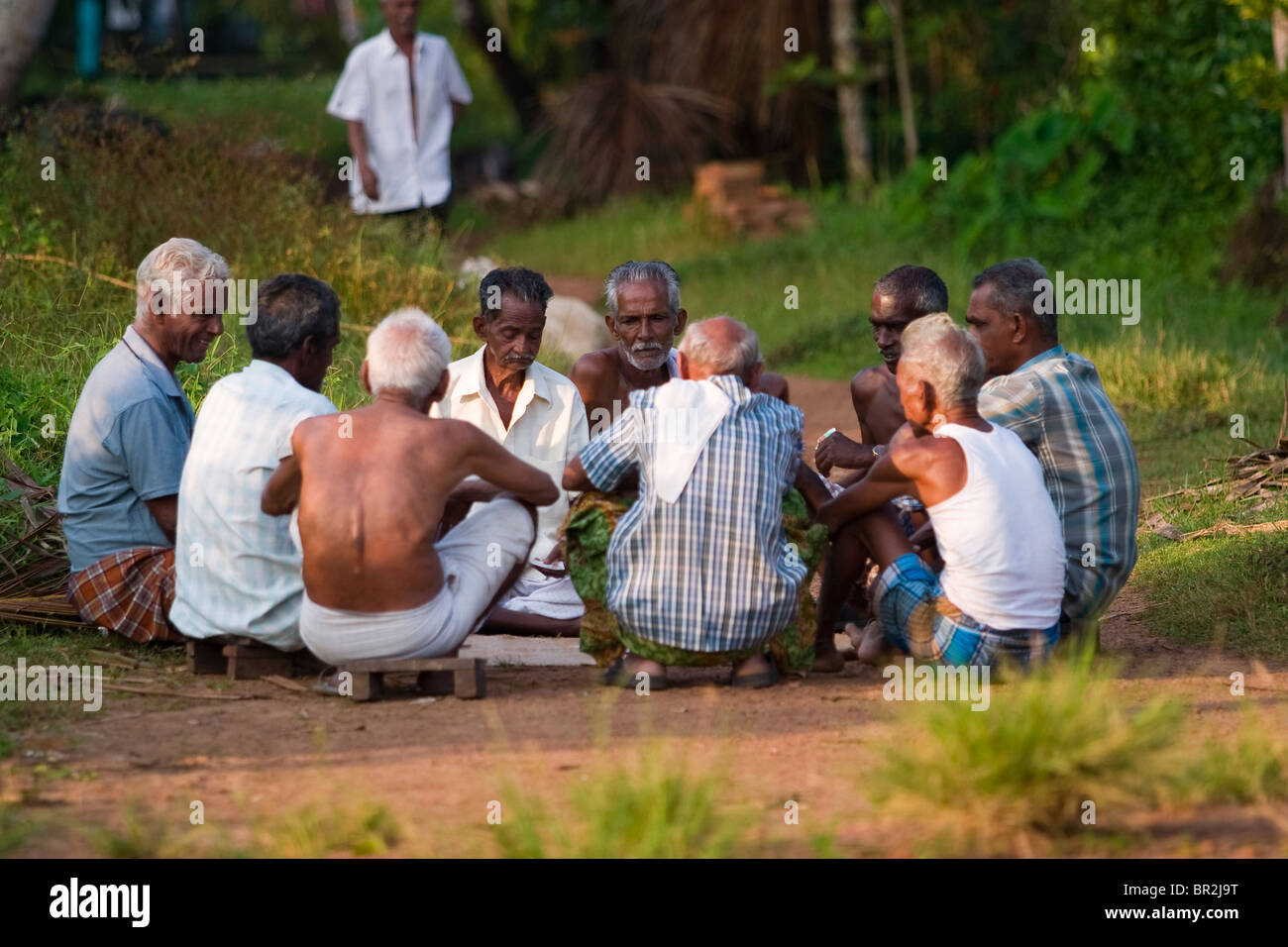 Gruppo di nove locale indiana uomini anziani seduti in cerchio su un suolo giocando a carte, Kerala backwaters, India. Foto Stock