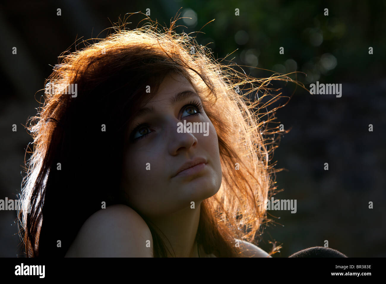 Headshot / Ritratto di un attraente dai capelli scuri giovane donna utilizzando il sole come retroilluminazione Foto Stock