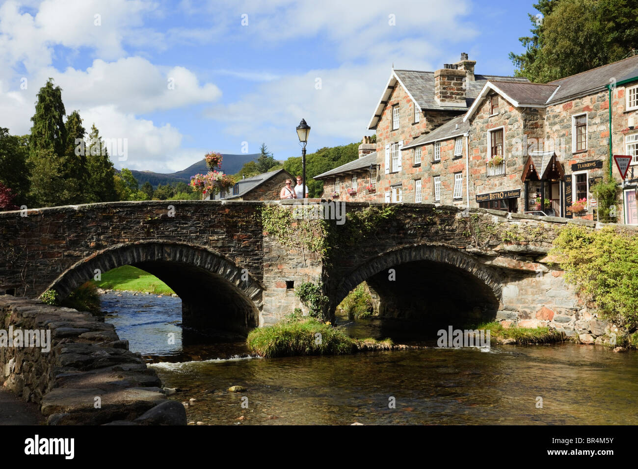 Vista lungo Afon Colwyn fiume al vecchio ponte ad arcate in Snowdonia village center. Beddgelert, Gwynedd, il Galles del Nord, Regno Unito, Gran Bretagna. Foto Stock