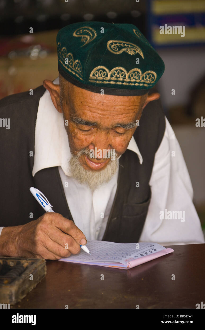 Uighur uomo doing business Prenota mantenendo, Hotan, Xinjiang, Cina Foto Stock