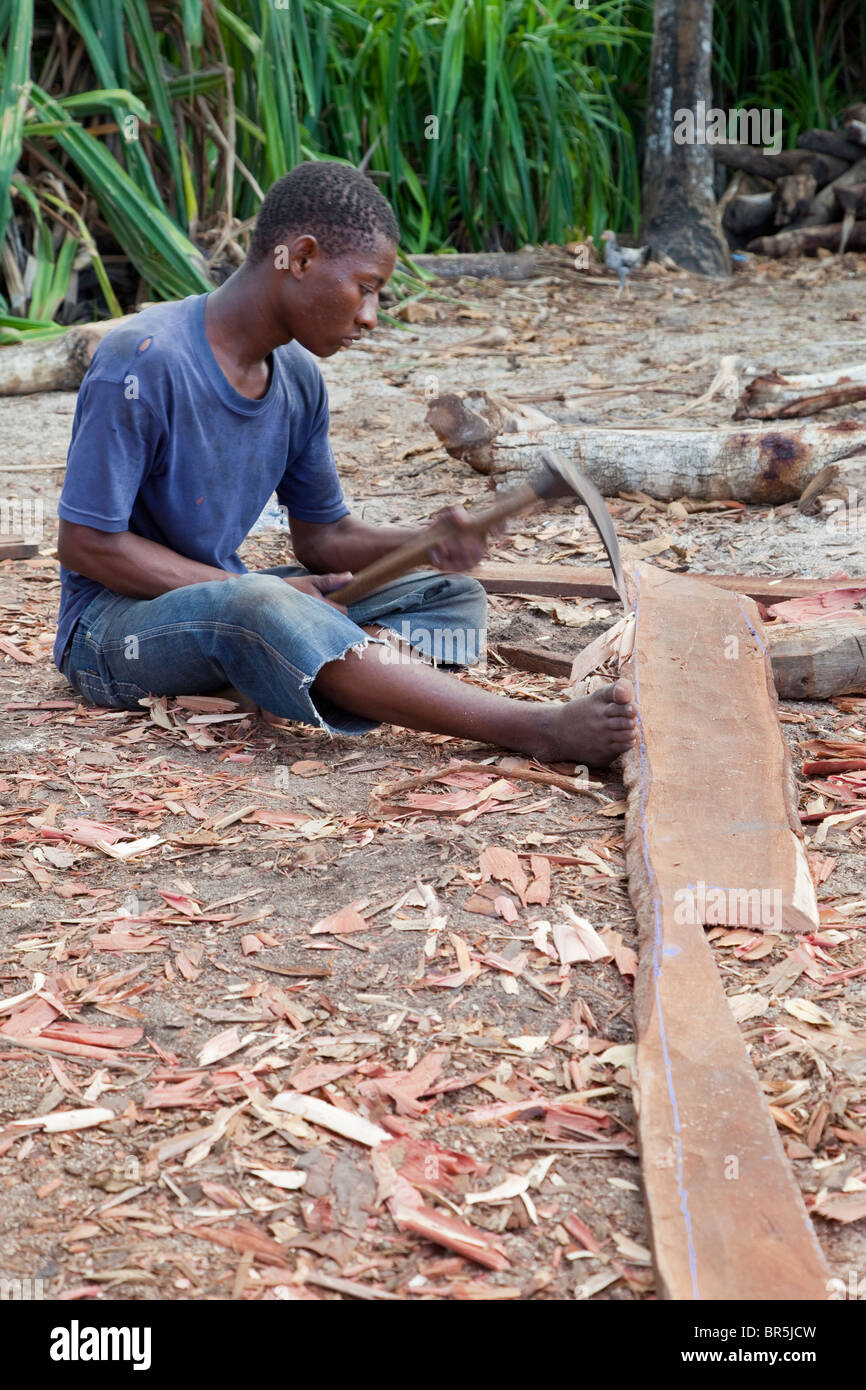 Nungwi, Zanzibar, Tanzania. Dhow Costruzione, Boat Building. Carpenter usando un Adze per smussare una doga. Foto Stock