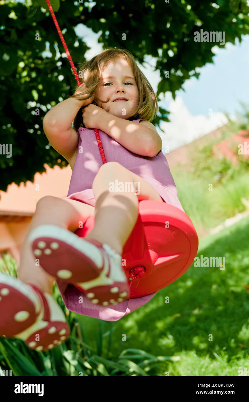 Felice piccola ragazza carina basculante in altalena nel giardino dietro la casa della famiglia Foto Stock