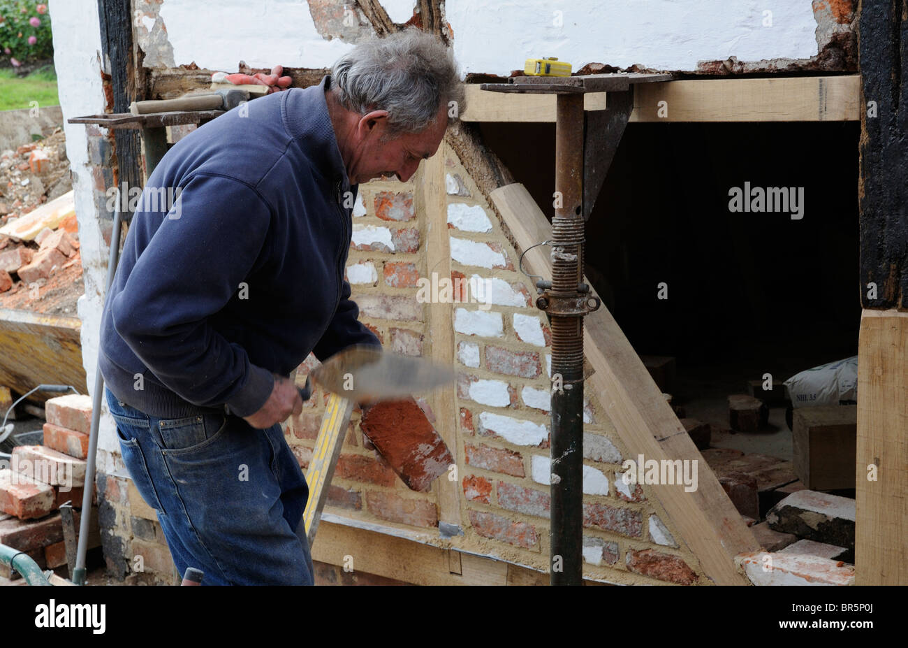 Il rinnovamento di un vecchio legno incorniciata edificio muratore utilizza una cazzuola a forma di un vecchio mattone Foto Stock