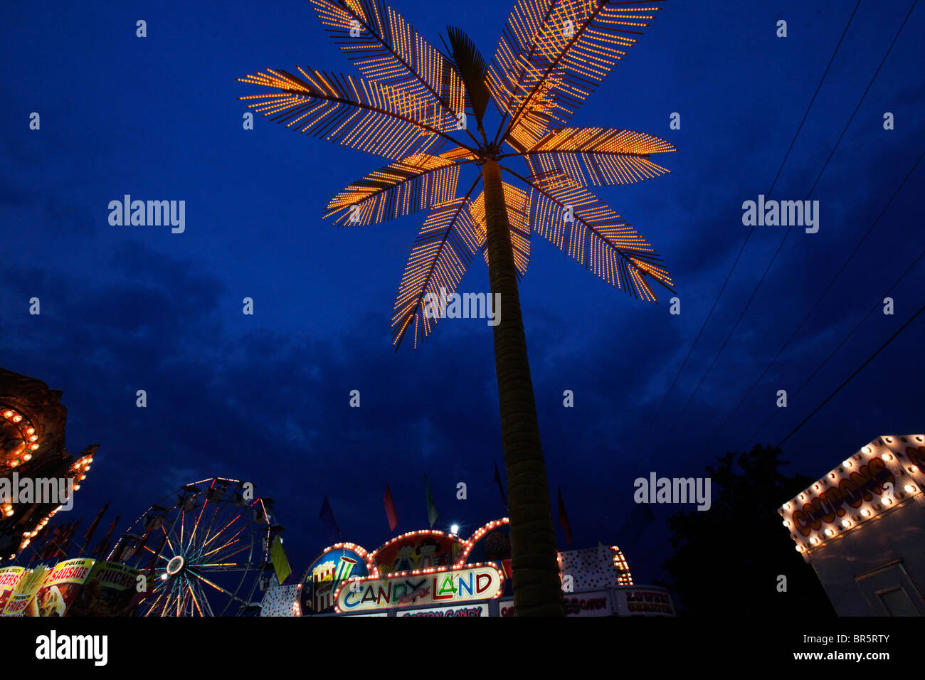 Palma illuminata e giostre al tramonto a Cape Girardeau, Missouri. Le luci festive si illuminano contro il cielo crepuscolo in fiera. Foto Stock