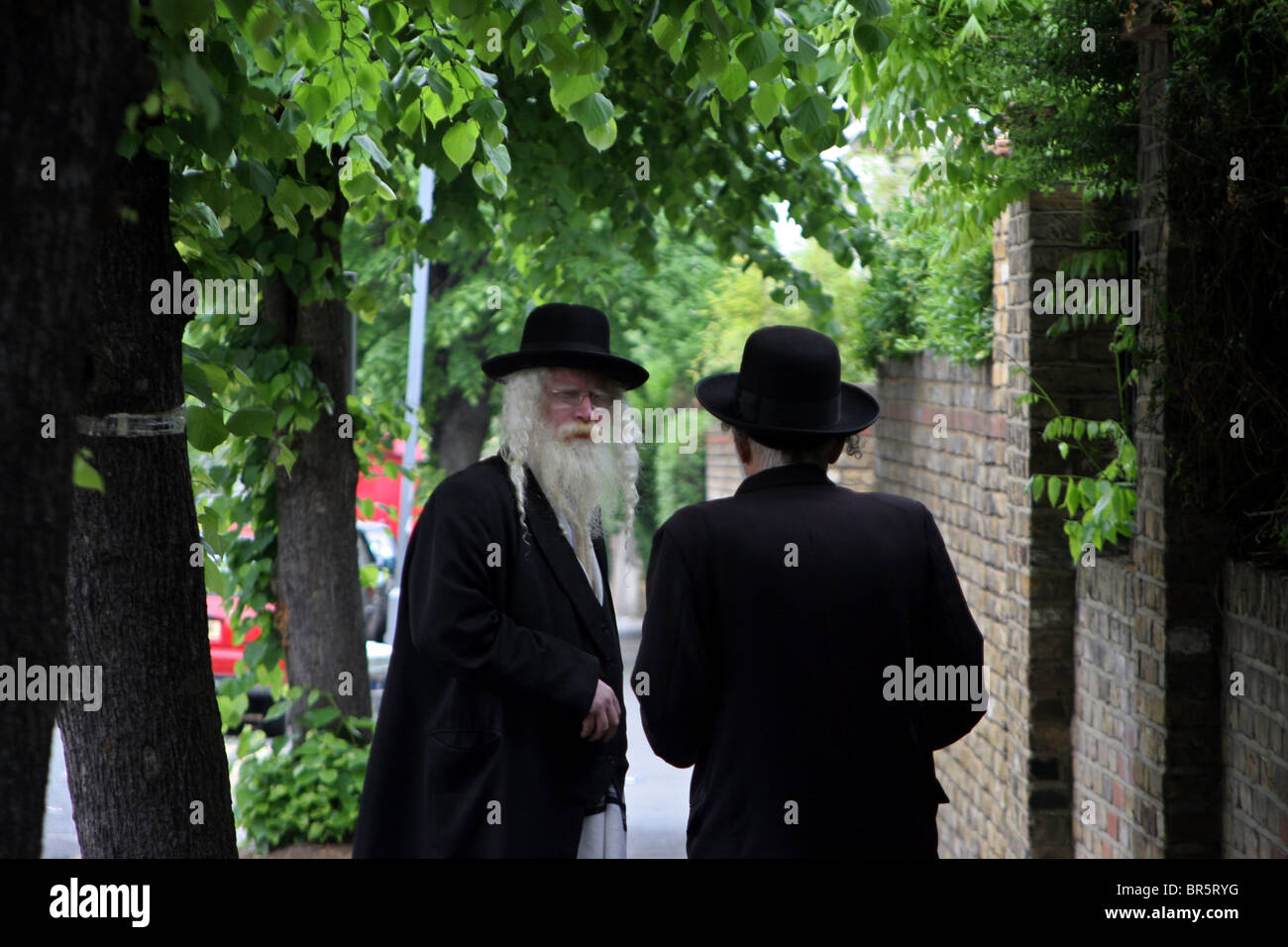 Due anziani ebrea ortodossa gli uomini con la barba vestita di nero  cappotti e cappelli in chat sulla pavimentazione di una strada alberata  Foto stock - Alamy