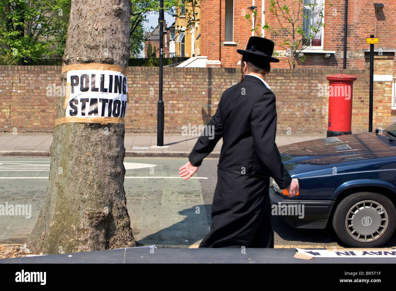 Un ebreo ortodosso uomo a camminare verso il basso Portland Avenue passato una Volvo e un segno per la locale stazione di polling nastrato a un albero. Foto Stock