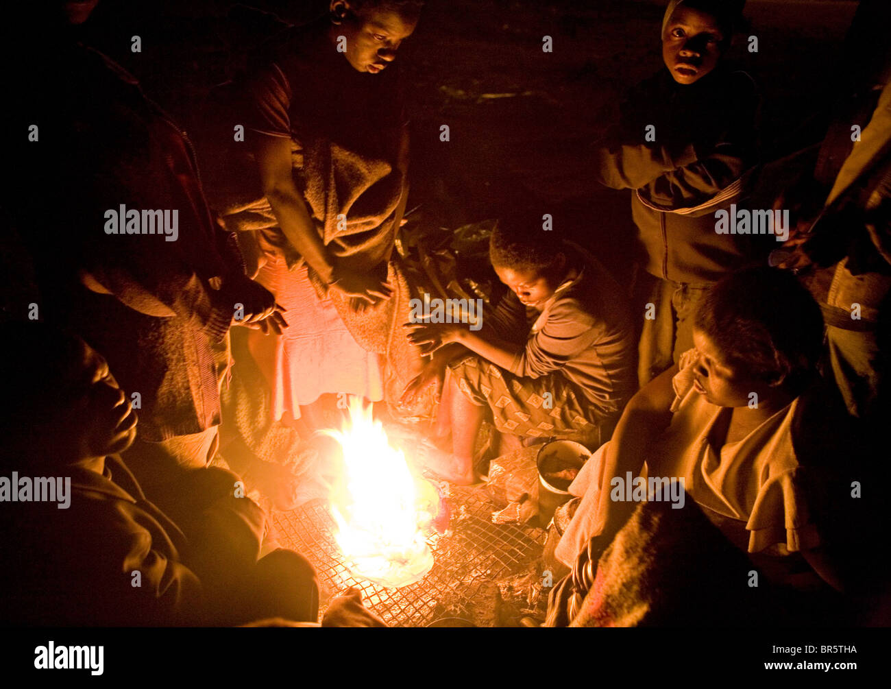 Un gruppo di gente di strada si raccolgono intorno ad un fuoco a uno di loro "basi" su una terra desolata di Harare, Zimbabwe. Foto Stock
