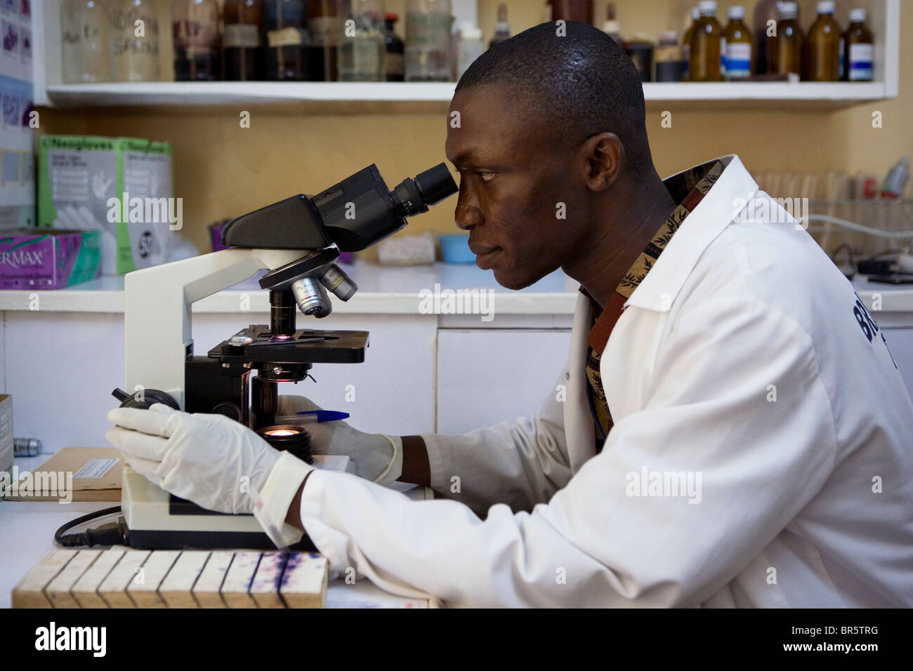 Tecnico di laboratorio guarda attraverso un microscopio, la ricerca attraverso i campioni di sangue per la Malaria. Afrikids Medical Center, Ghana Foto Stock