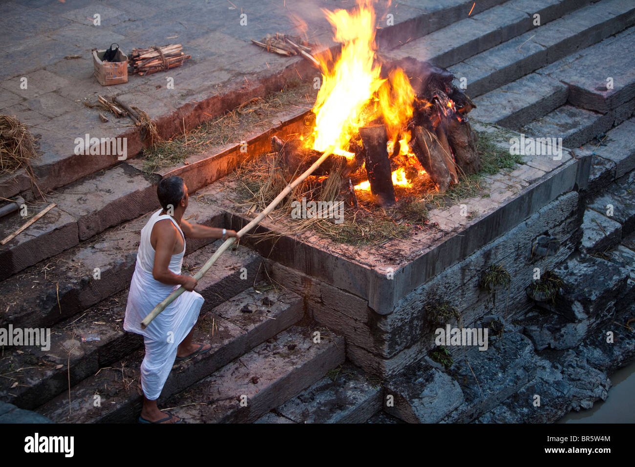 Uno dei dipendenti presso il Tempio di Pashupatinath a Kathmandu accende il fuoco pronto a bruciare i corpi per la cremazione. Foto Stock