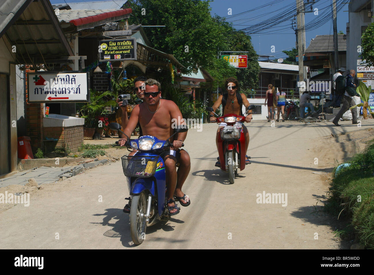 Gli occidentali ride scooter attraverso le strade di Hat Rin, Koh Phangnan, Thailandia Foto Stock