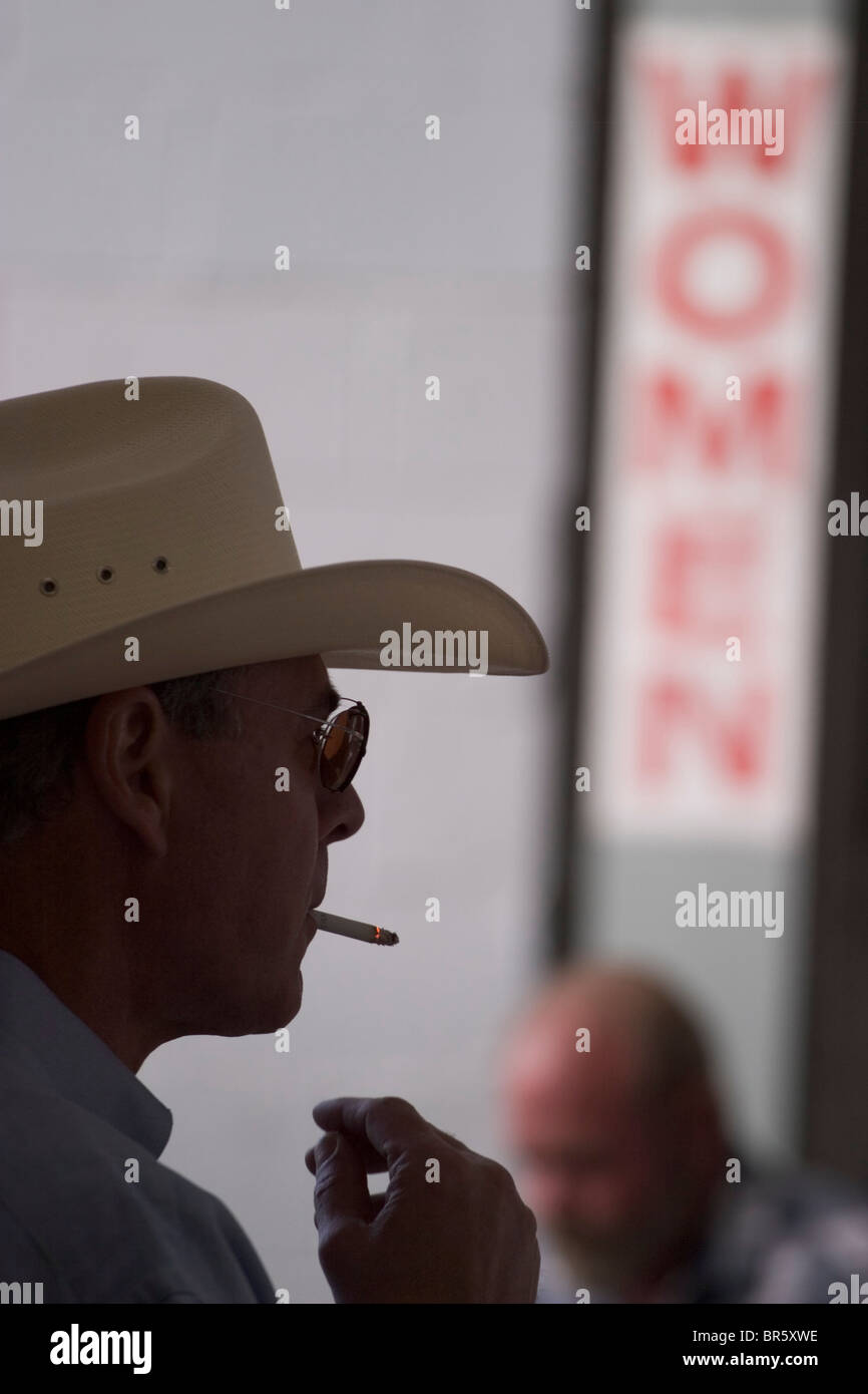 Vestito da cowboy e ingranaggio di sigarette su un ventilatore in piedi accanto a una donna restroom Foto Stock