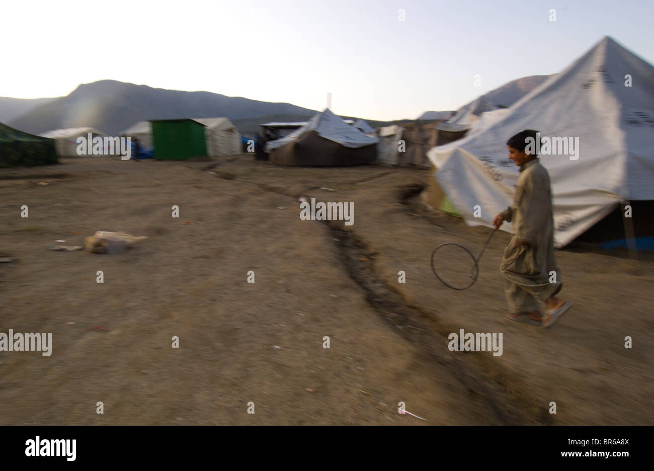 Un bambino gioca con un cerchio e il bastone fra le tende presso la Meira camp per i superstiti del terremoto Provincia di Frontiera di Nordovest Pakista Foto Stock