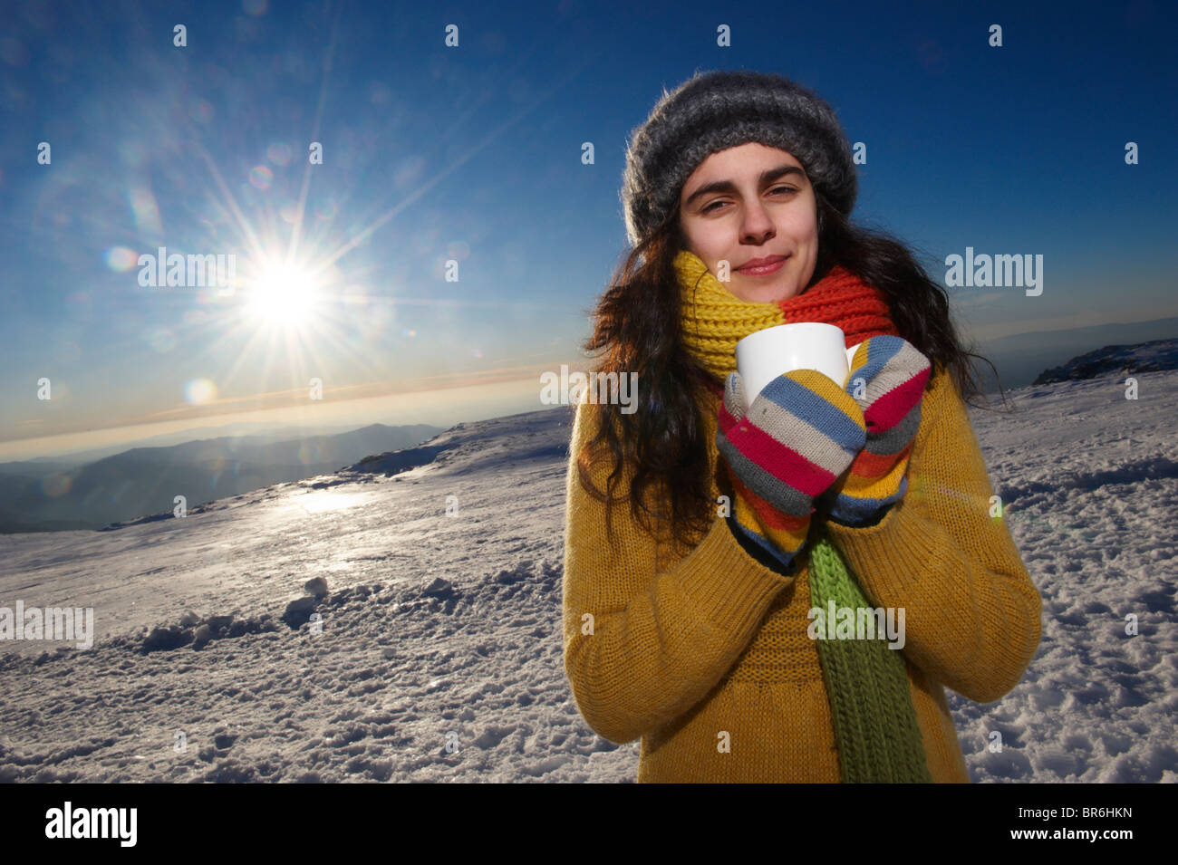 Un sorridente giovane donna detiene una tazza di cioccolato caldo nella neve, ritratto Foto Stock