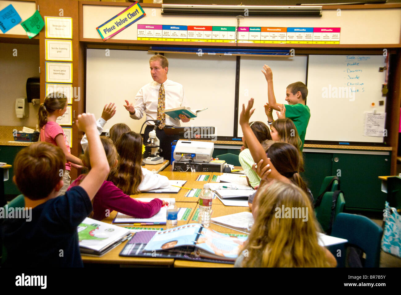 Gli studenti' mani andare fino in risposta a una domanda come una scuola media insegnante conduce un entusiasta di classe a San Clemente, CA. Foto Stock