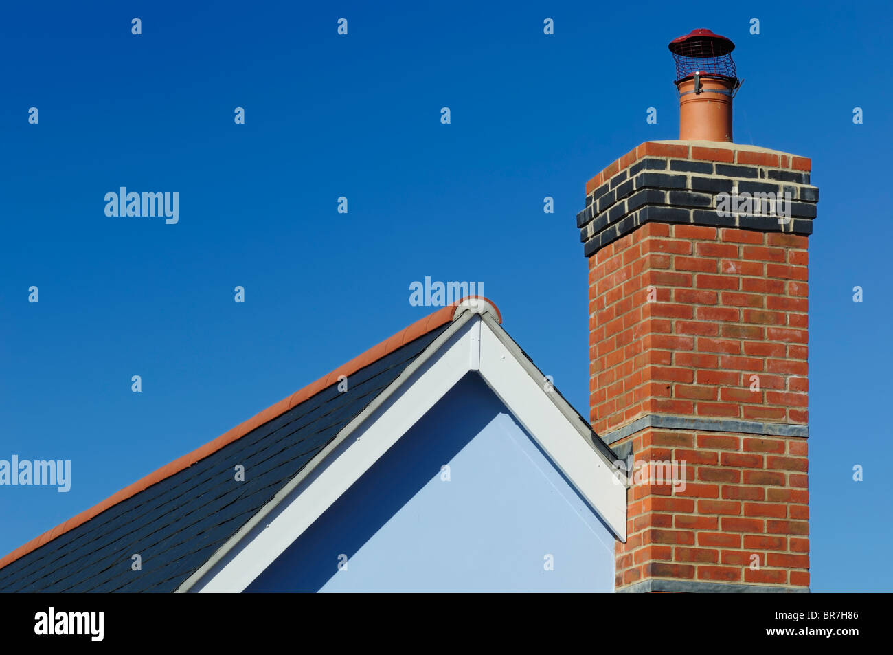 Una vista ravvicinata di una ciminiera in mattoni su una casa, sotto un cielo blu chiaro. Foto Stock