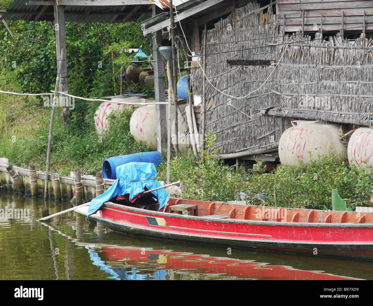 Longtail in legno barca su un canale nella parte anteriore della tradizionale casa di paglia in Thailandia. Foto Stock