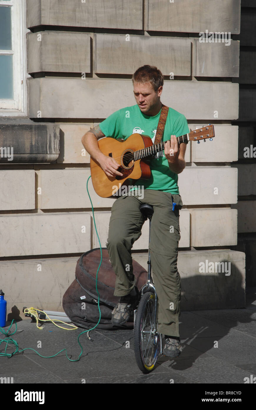 Un suonatore ambulante suona la chitarra mentre in equilibrio su un monociclo su High Street di Edimburgo, in Scozia. Foto Stock