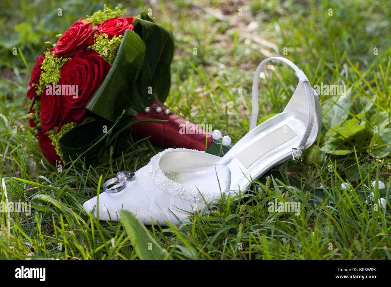 Simboli di nozze in erba. Anelli, boquet e bianco tacco alto scarpa. Foto Stock