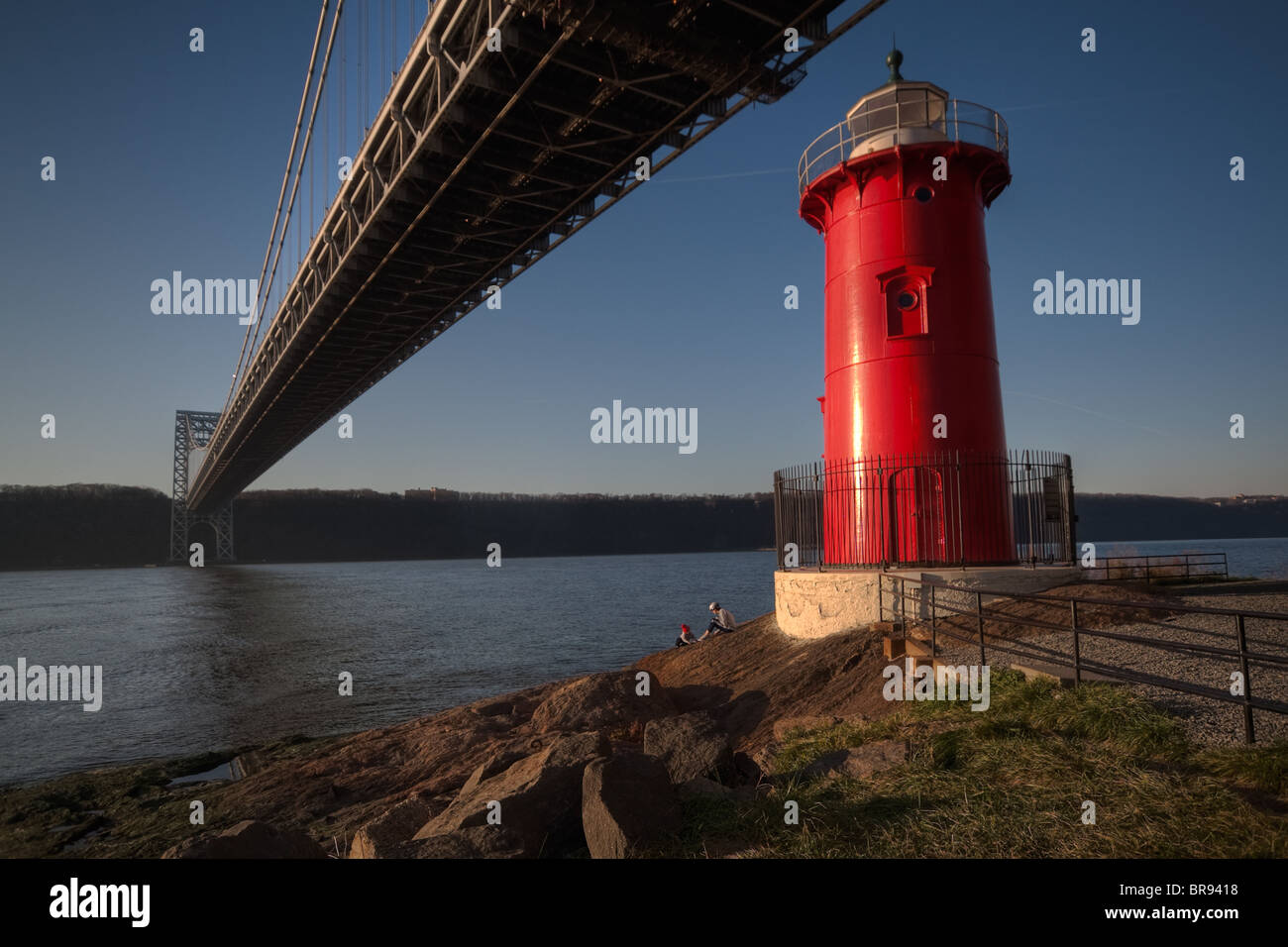 Un padre e figlio sedersi accanto al faro rosso piccolo sotto il Ponte George Washington Bridge al tramonto Foto Stock