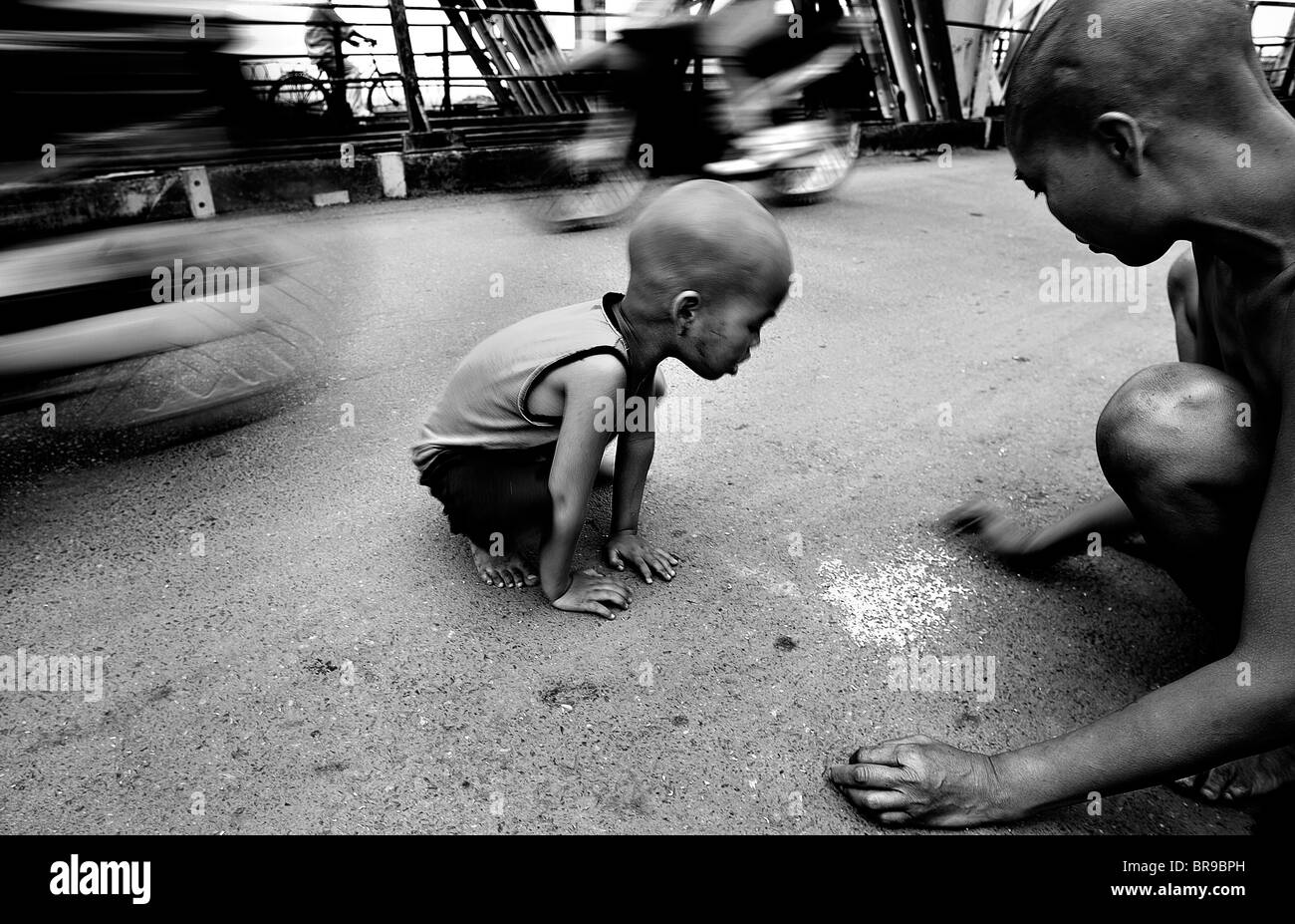 Madre riprende il riso sulla strada mentre il figlio di orologi in Hanoi Vietnam. Foto Stock