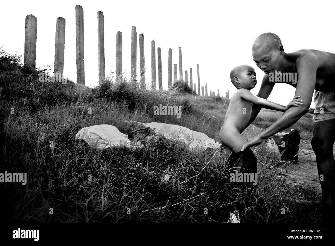 Madre aiuta a mettere il figlio di abbigliamento su Red River Vietnam Foto Stock