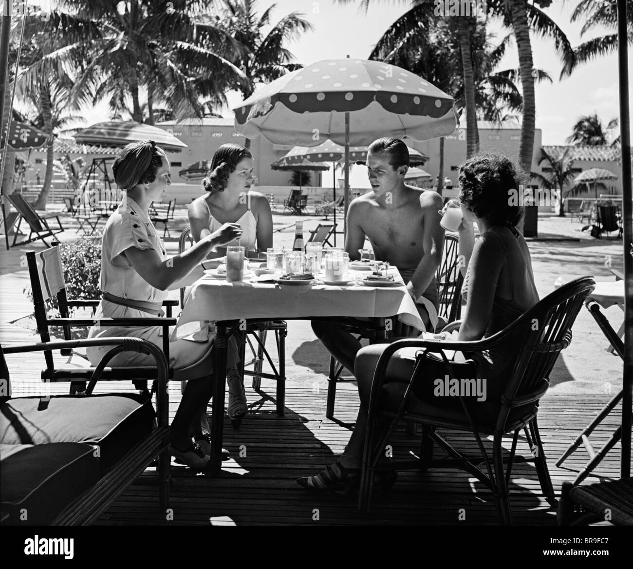 1930s tre donne e un uomo seduto in piscina tropicale tabella parlare insieme Foto Stock