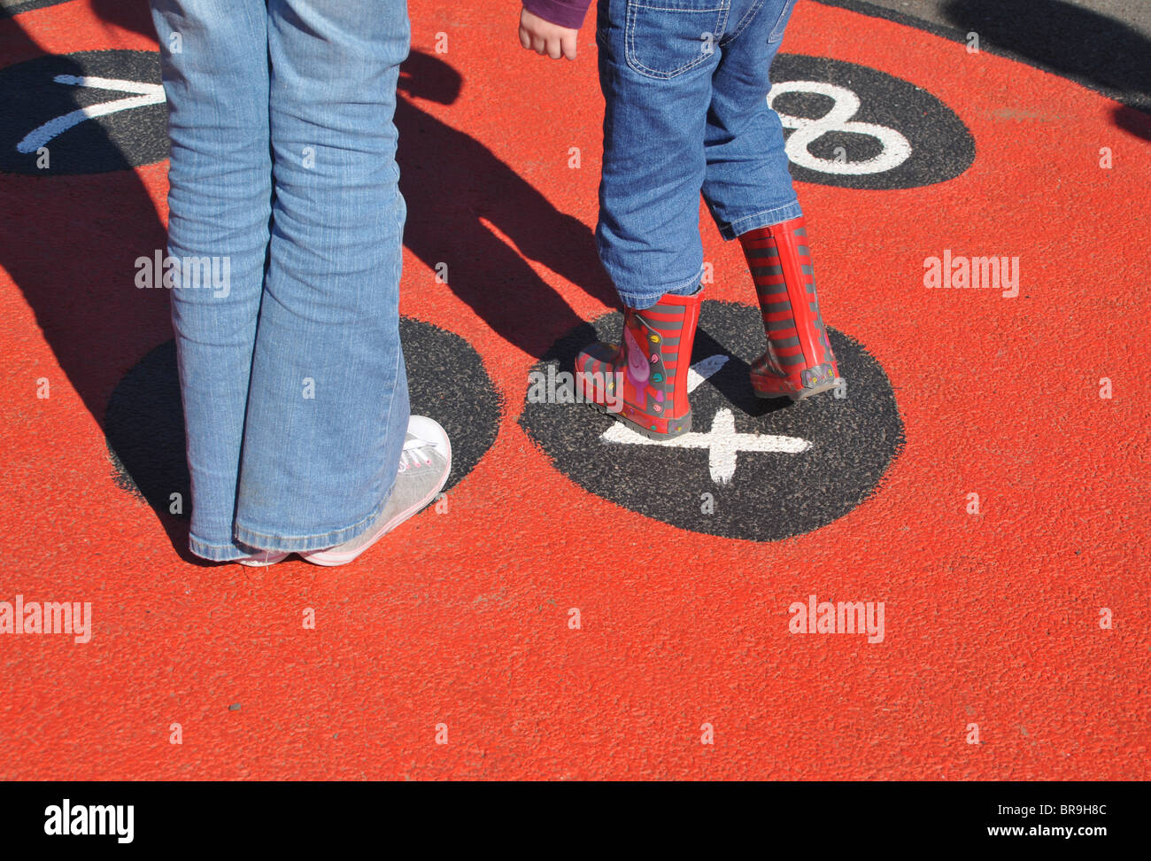 Un dettaglio dei bambini con i piedi sul un rosso hop scotch coccinella dipinta nel parco giochi di una scuola vivaio. Foto Stock