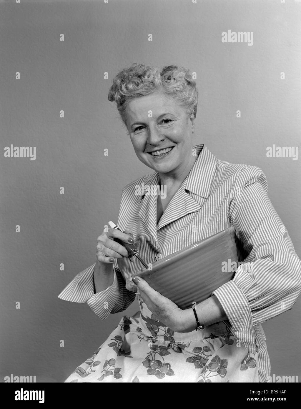 Negli anni quaranta anni cinquanta donna sorridente casalinga tenendo un recipiente di miscelazione guardando la fotocamera Foto Stock