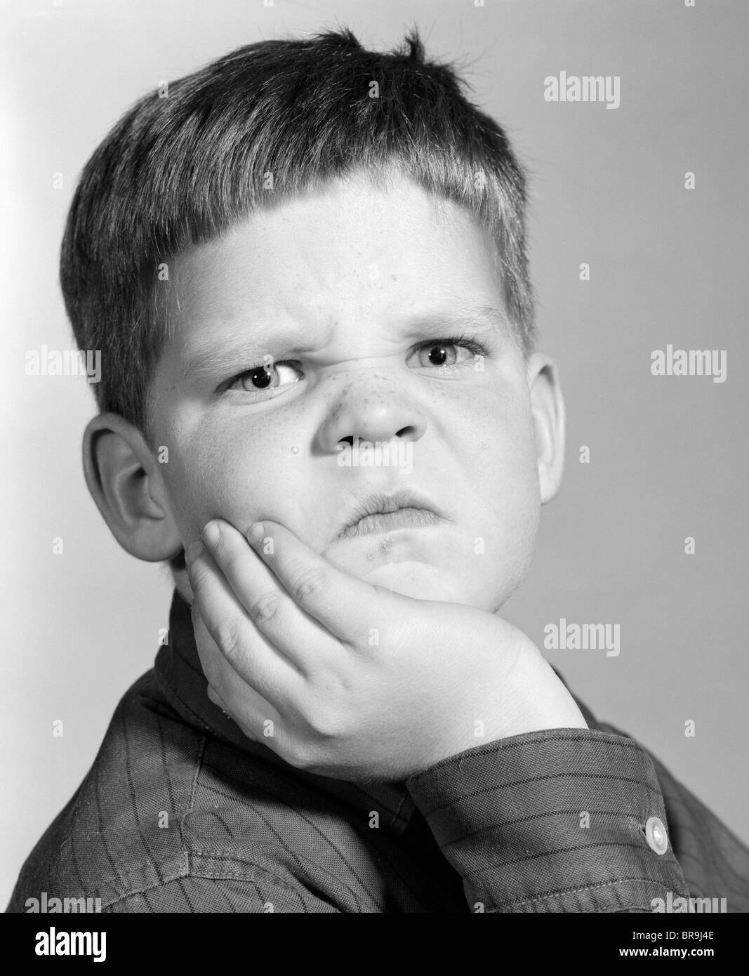 Anni sessanta Little Boy rendendo arrabbiato funny espressione facciale guardando la fotocamera Foto Stock