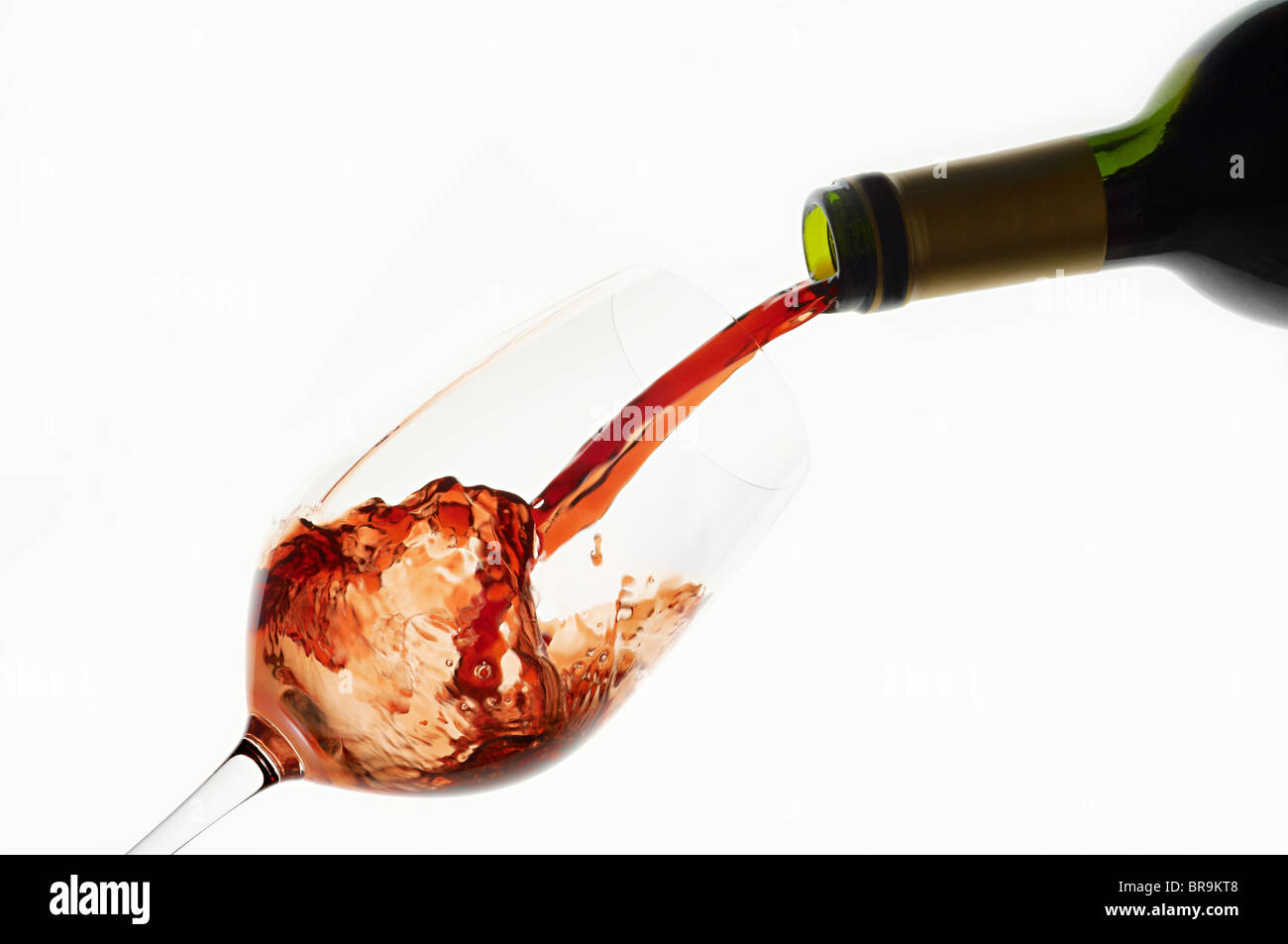 Bottiglia di vino rosso che viene versato nel bicchiere da vino e schizzi Foto Stock