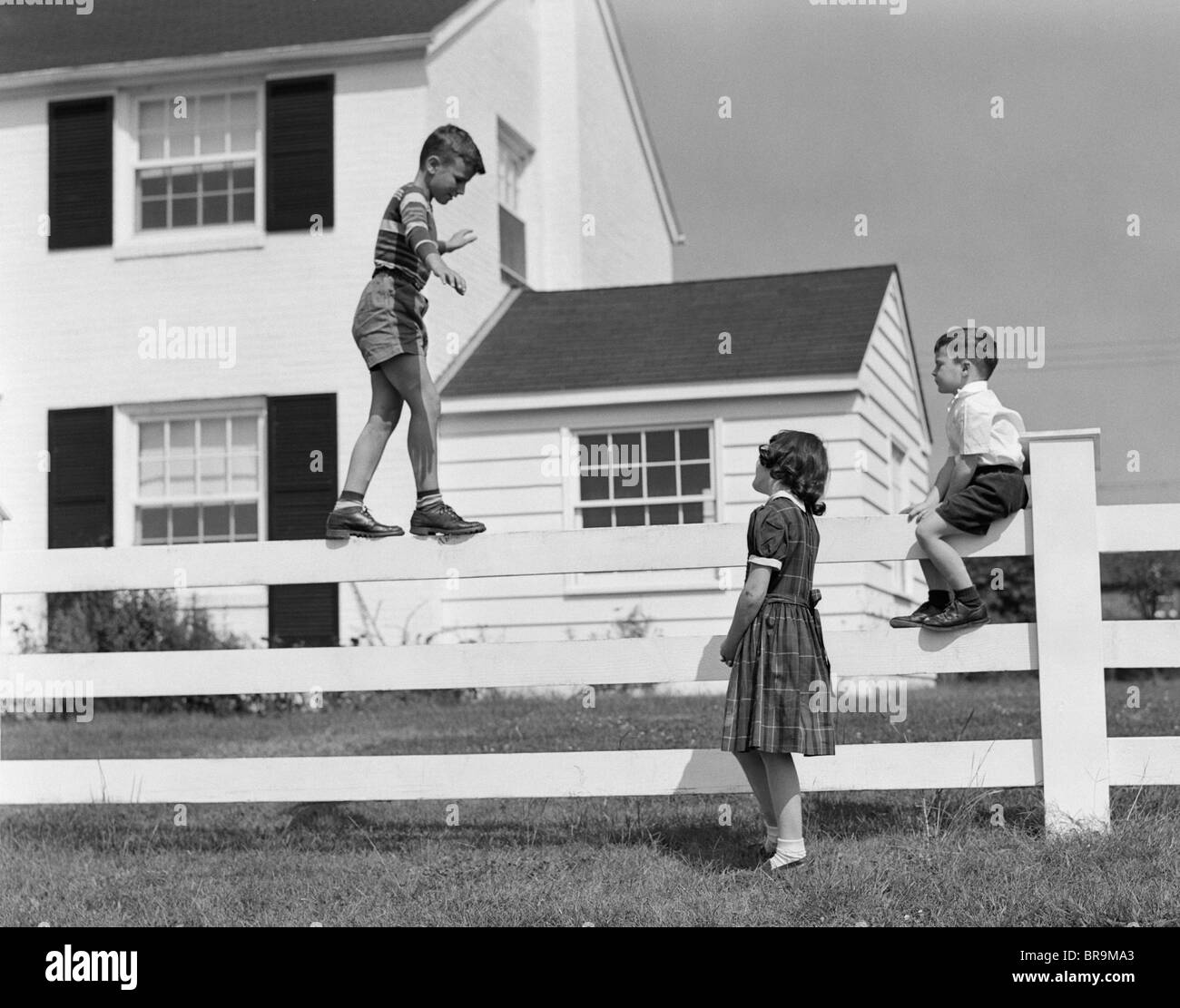Anni Cinquanta BOY A PIEDI sul bilanciamento del recinto altri bambini stando seduti accanto alla recinzione Foto Stock
