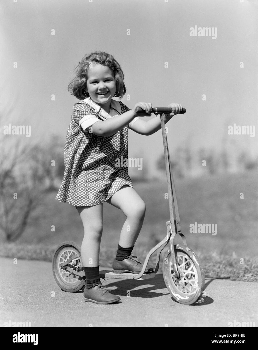 1930s ragazza che gioca sul marciapiede di scooter a sorridere guardando la fotocamera Foto Stock