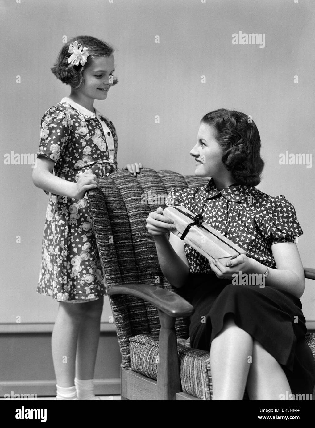 1930s ragazza dando donna seduta nella poltrona di un presente Foto Stock