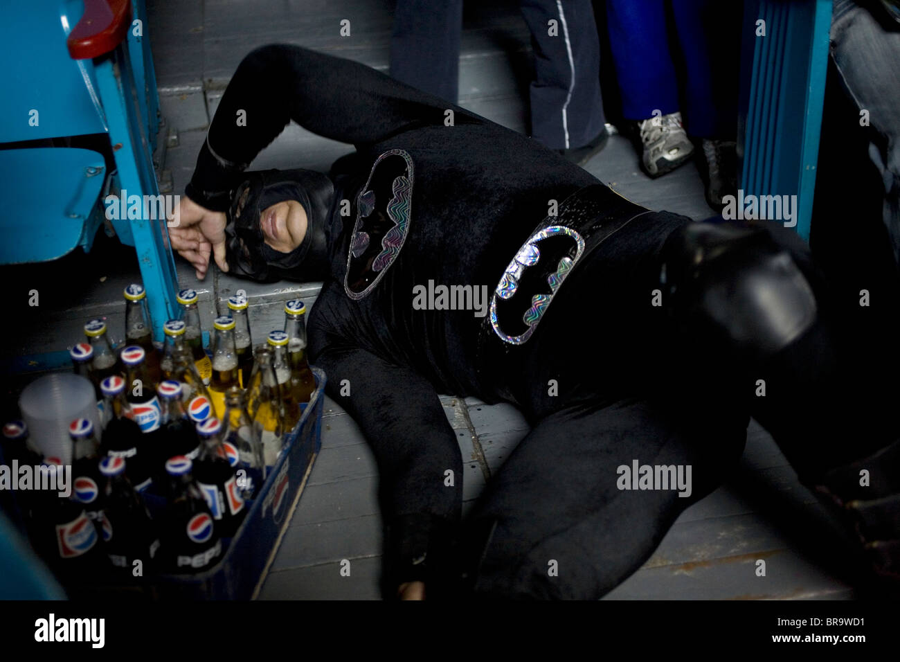 Un wrestler mascherato come il supereroe Batman giace sul pavimento vicino a spettatori a Lucha Libre evento Foto Stock