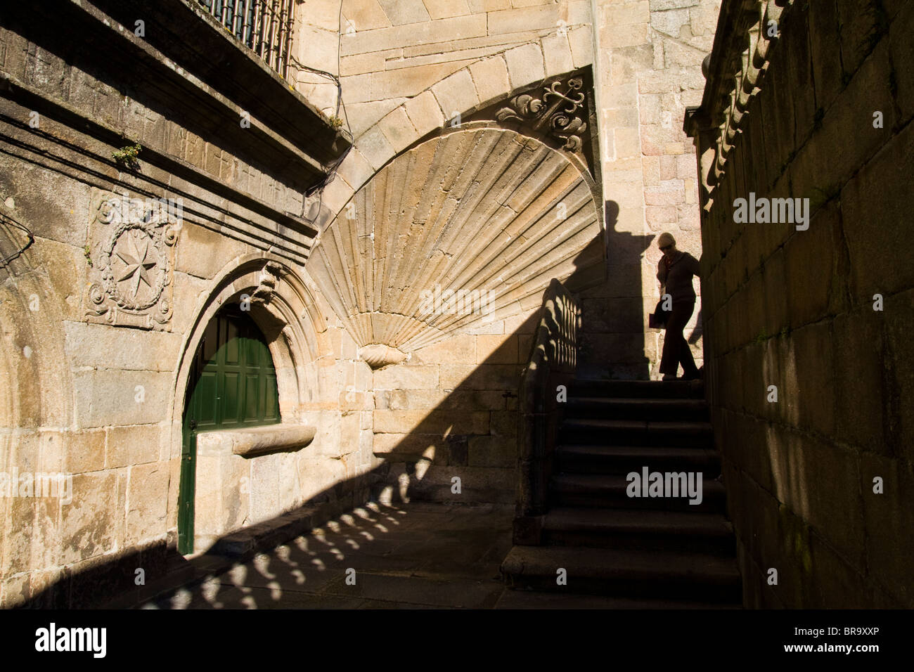 Una donna cammina giù per le scale che conducono fuori della cattedrale e passato un grande scaloppina al simbolo della shell di Saint James. Foto Stock