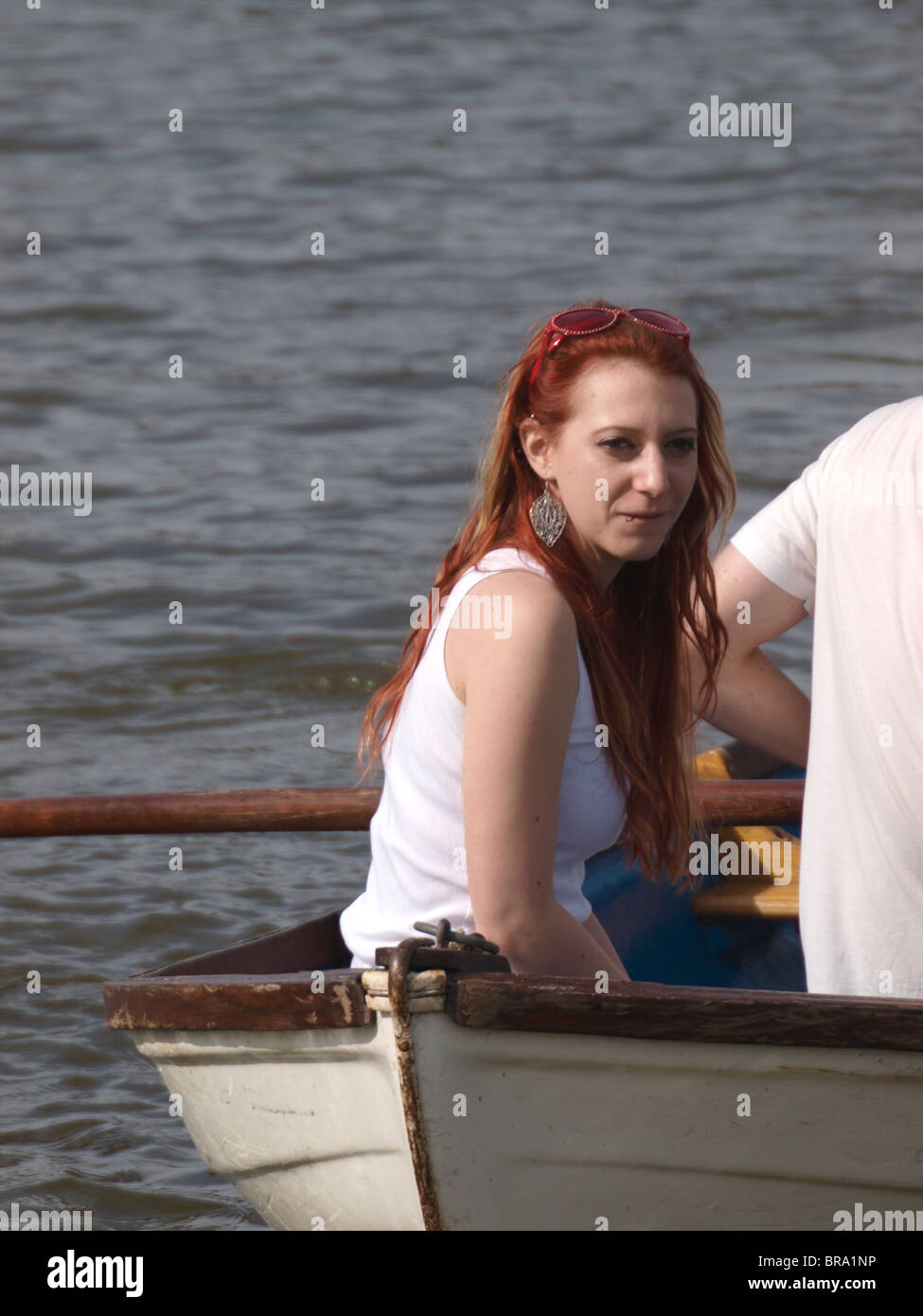 Rosso giovane donna dai capelli nella parte anteriore della barca a remi, Cornwall, Regno Unito Foto Stock