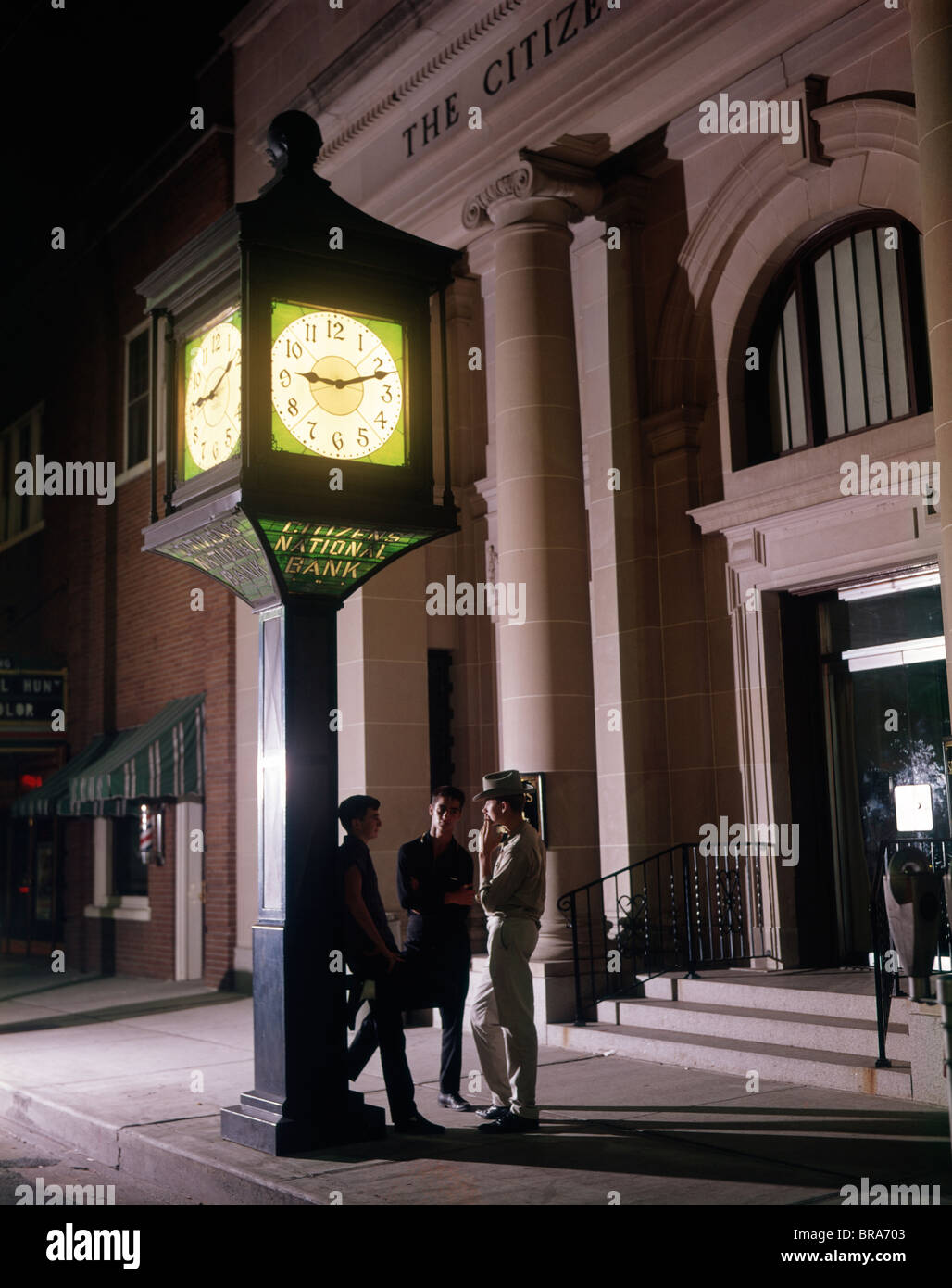 1960 anni sessanta retrò 3 ragazzi adolescenti orologio permanente al di fuori del palazzo della banca di fumare sigarette Foto Stock