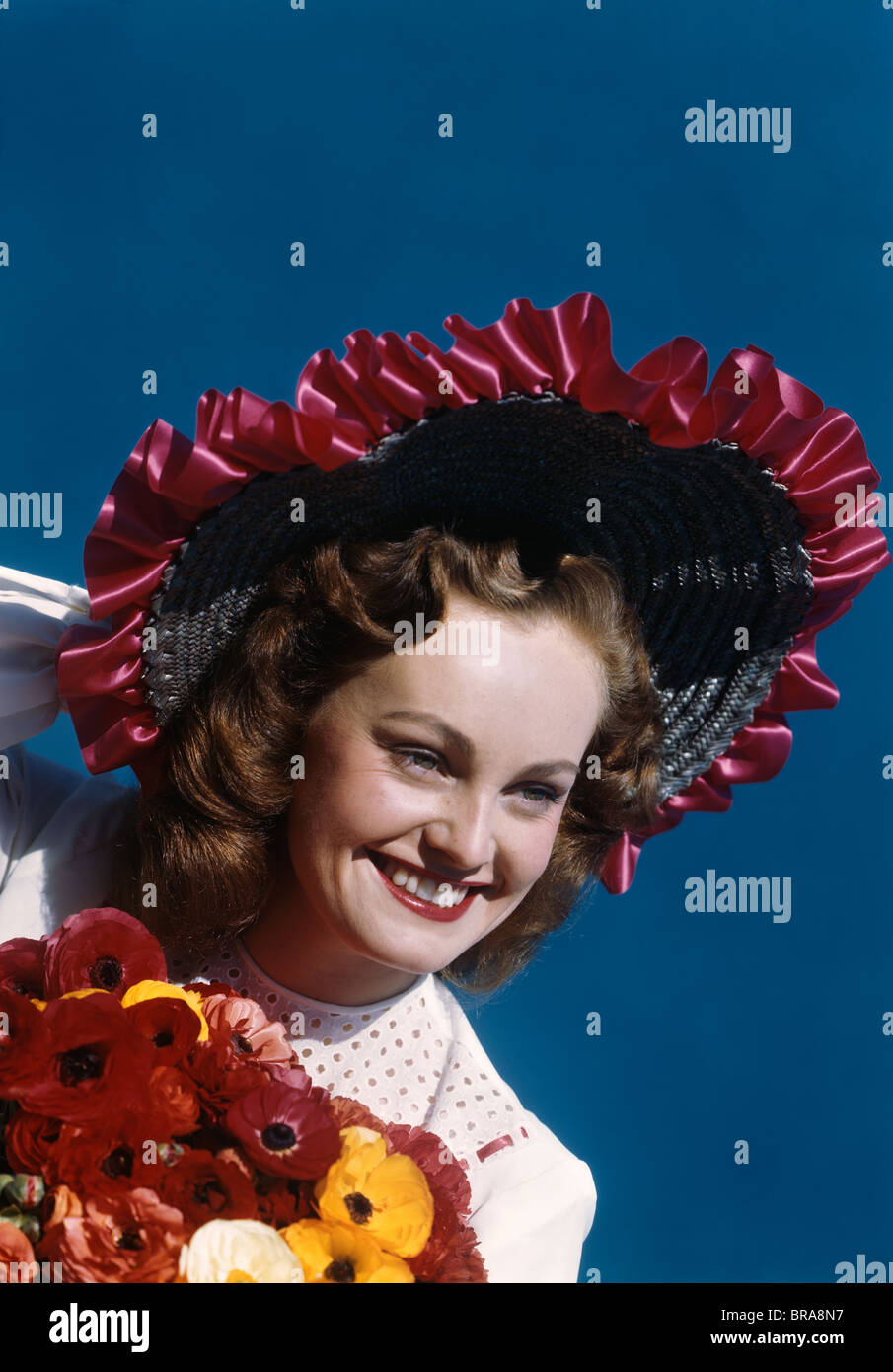Negli anni quaranta anni cinquanta ritratto di donna sorridente indossando ampia colmato cappello di paglia con nastro HOLDING bouquet di papaveri Foto Stock
