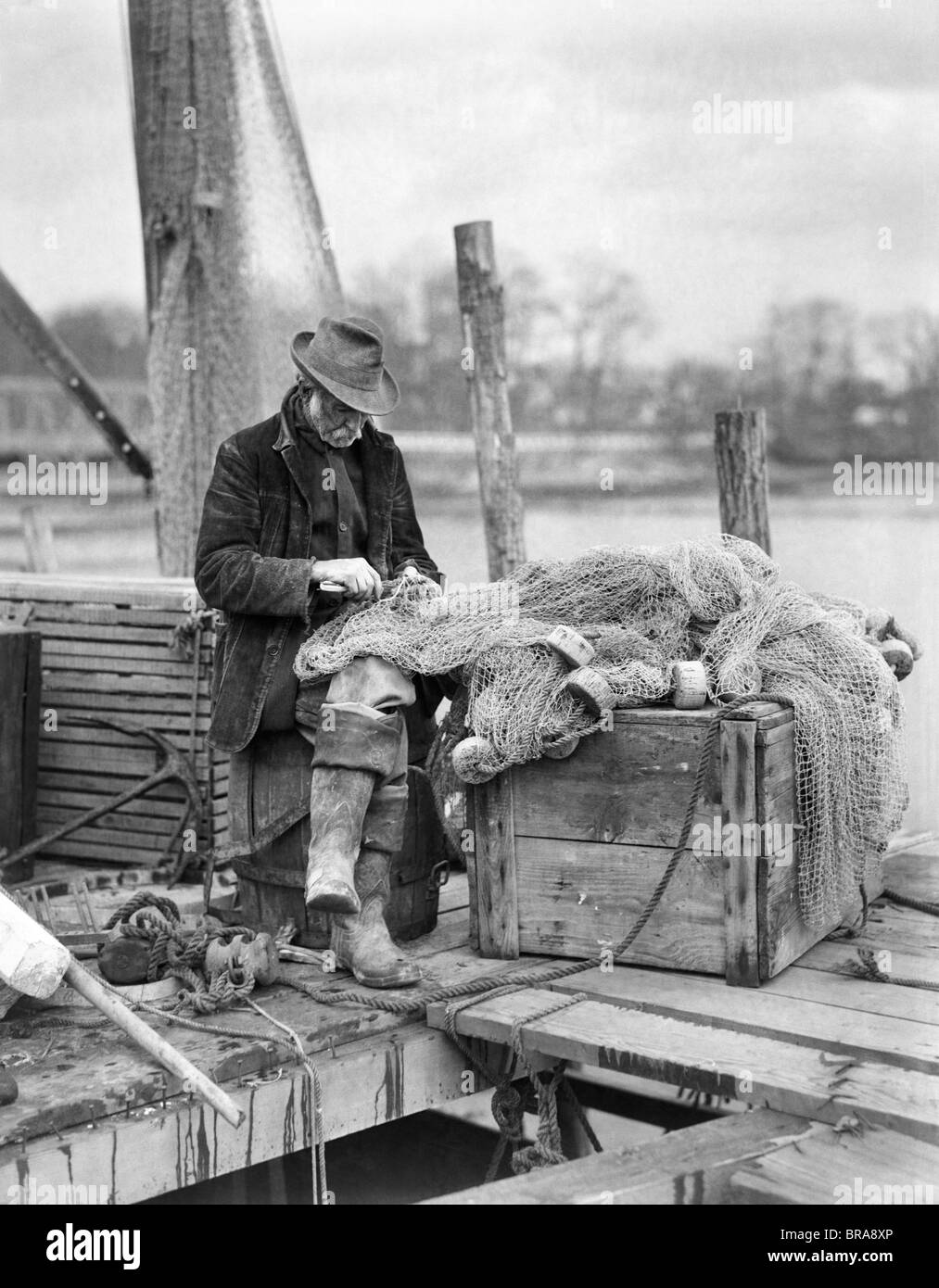 1910s uomo vecchio pescatore RIPARAZIONE DI RETI DA PESCA SUL DOCK WESTPORT CONNECTICUT Foto Stock